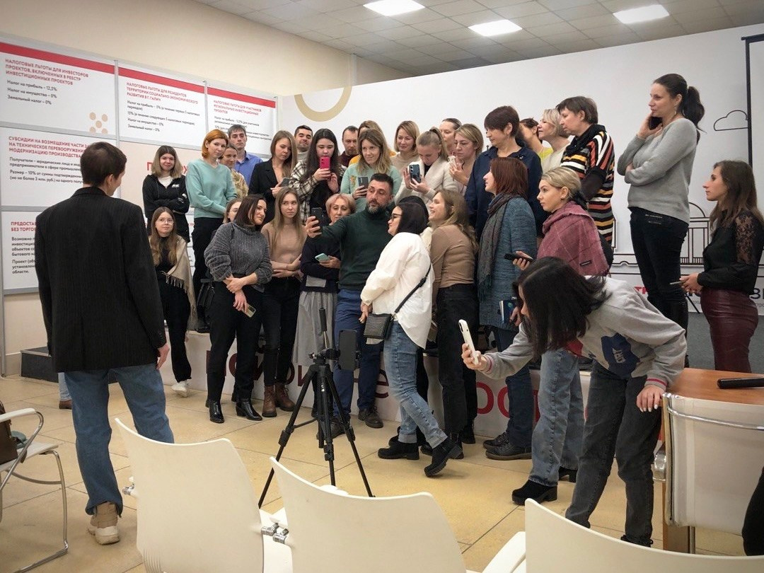 Много людей стоят вокруг Руслана Шихалиева, который показывает настройки камеры