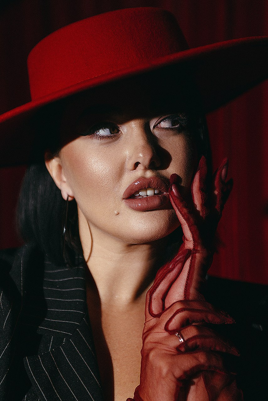 Крупный портрет девушки в красной шляпе с красными перчатками и красной помадой.