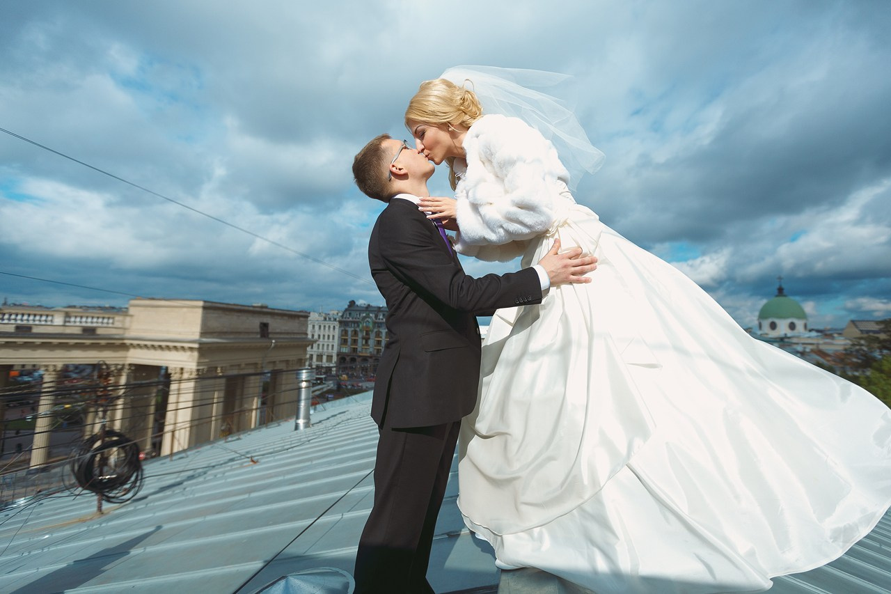 жених в черном костюме целует невесту в пышном платье на крыше дома в Петербурге