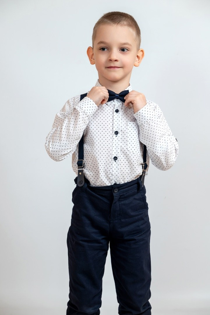 Стиляга из детского сада держится за бабочку руками позируя фотографу.