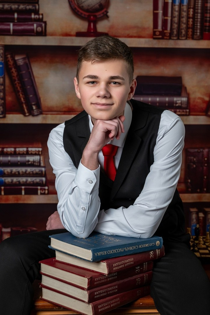 Парень облокотившись на стопку учебников красиво улыбается фотографу.