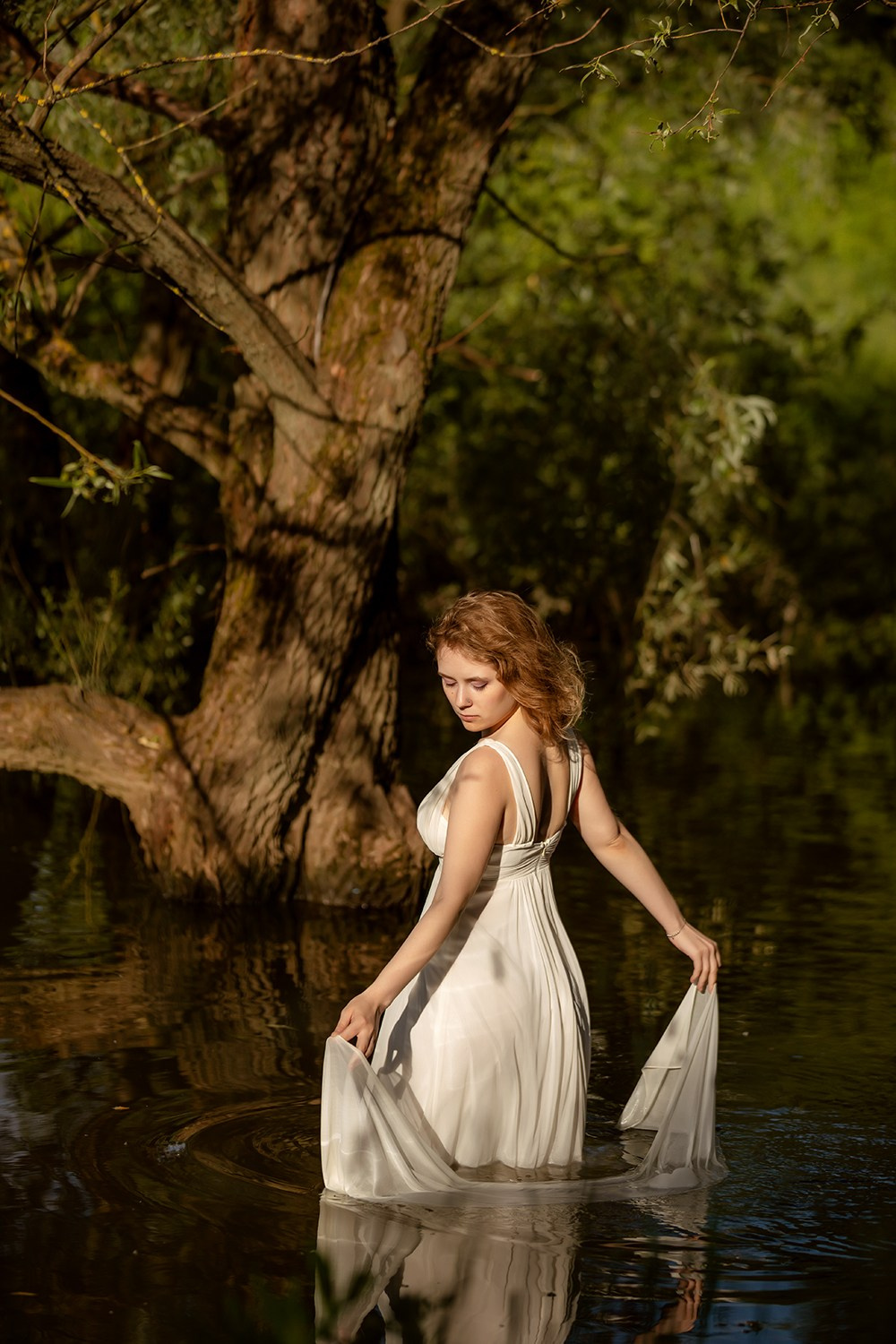 Девушка в белом платье стоит по колено в воде сказочного пруда