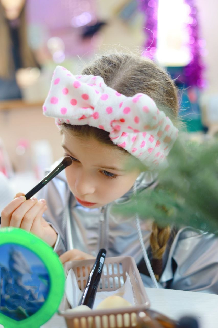 Девочка 9 лет пробует с помощью кисти сделать макияж глаз, используя сухие тени