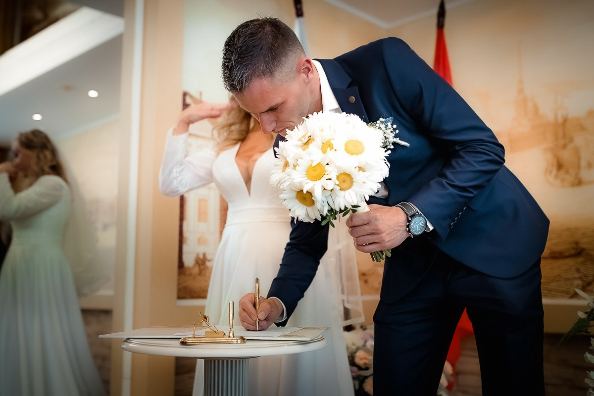Жених ставит роспись во время регистрации брака в ЗАГСе на Васильевском острове в Санкт-Петербурге.  Горизонтальный поясной кадр.