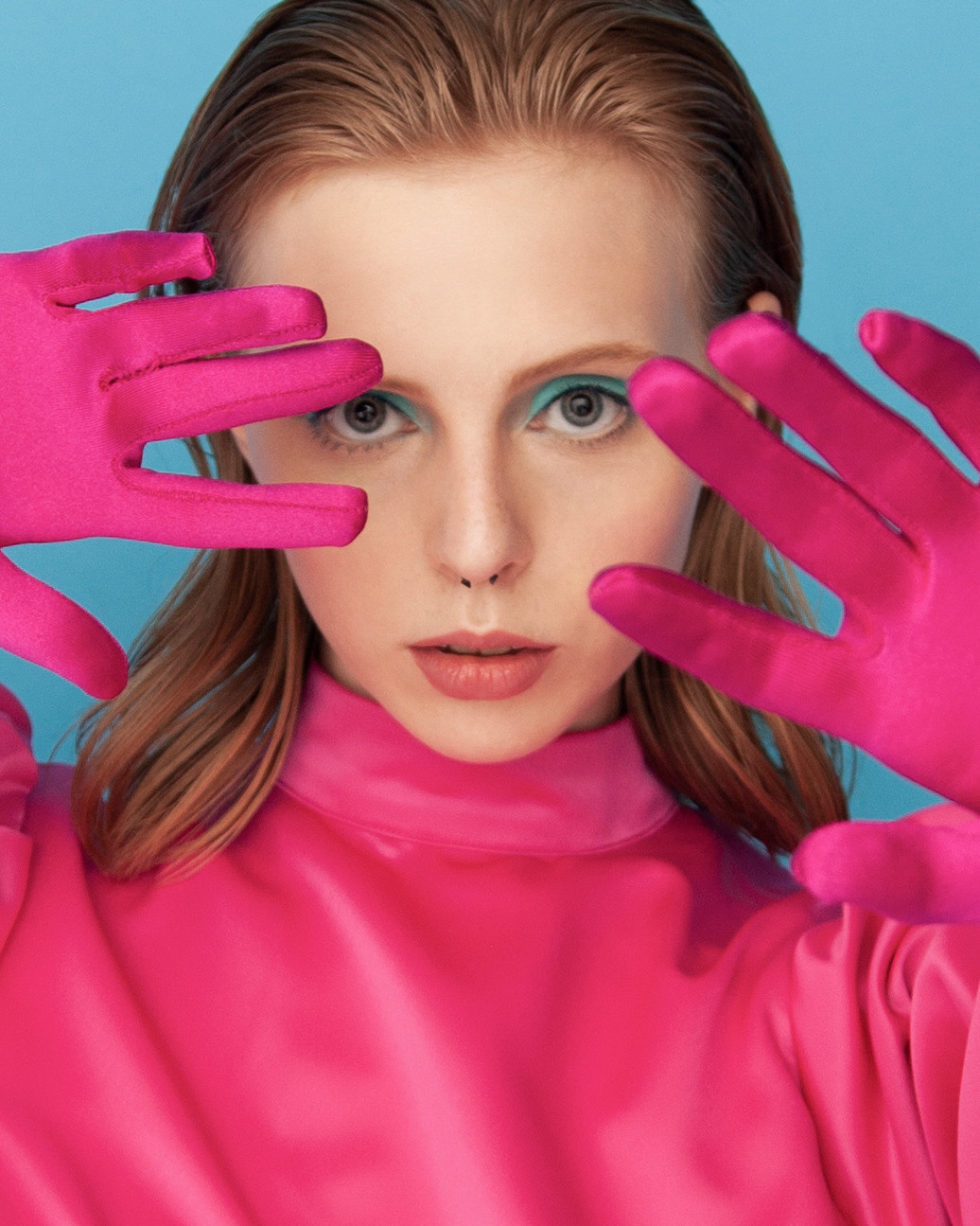 Портрет рыжей девушки, прекрывающая лицо розовыми перчатками.