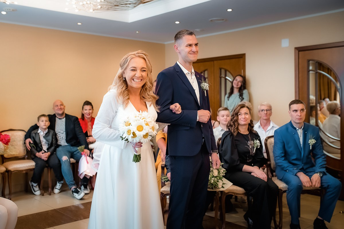 Жених и невеста стоят и смотрят на регистратора во время регистрации брака в ЗАГСе на Васильевском острове в Санкт-Петербурге. Невеста смеётся. Горизонтальный поясной кадр.