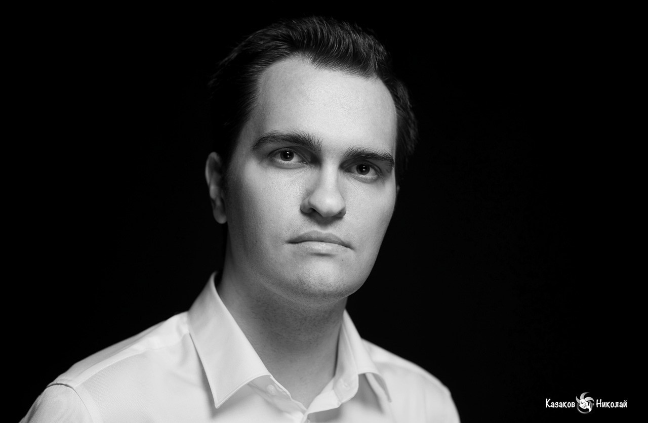 Черно-белый портрет серьезного мужчины в темной комнате.