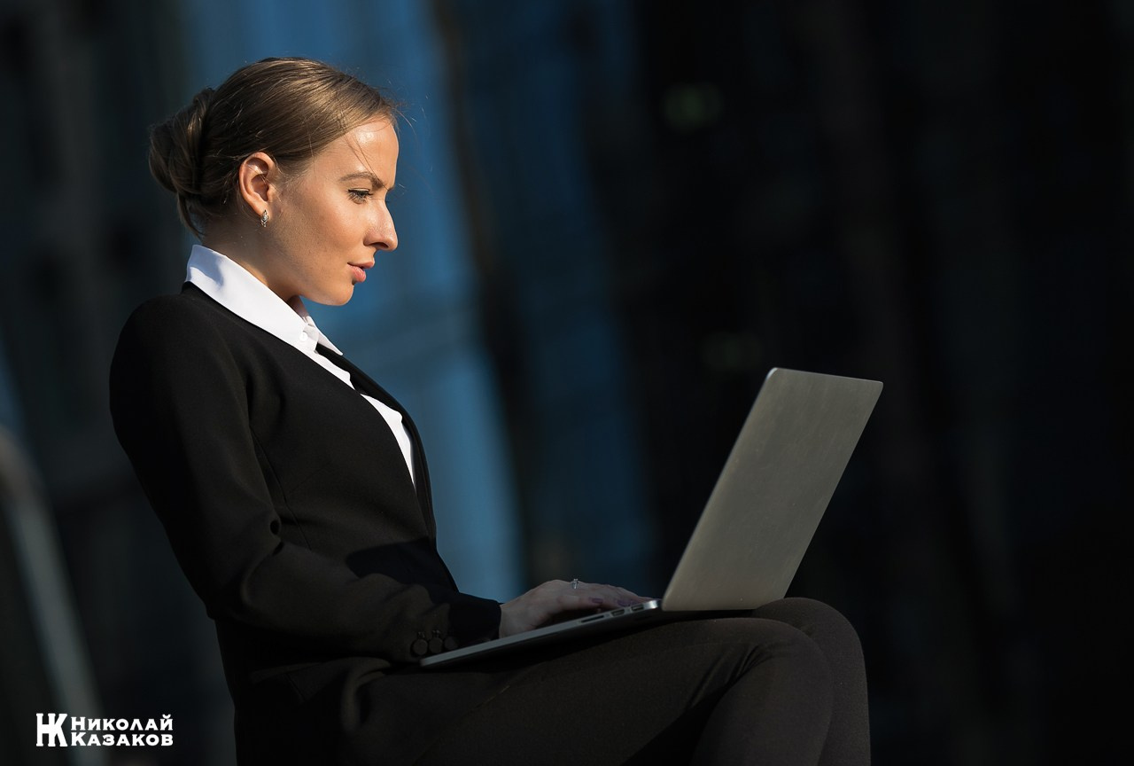 Деловая молодая женщина работает на ноутбуке на улице на фоне бизнес центра