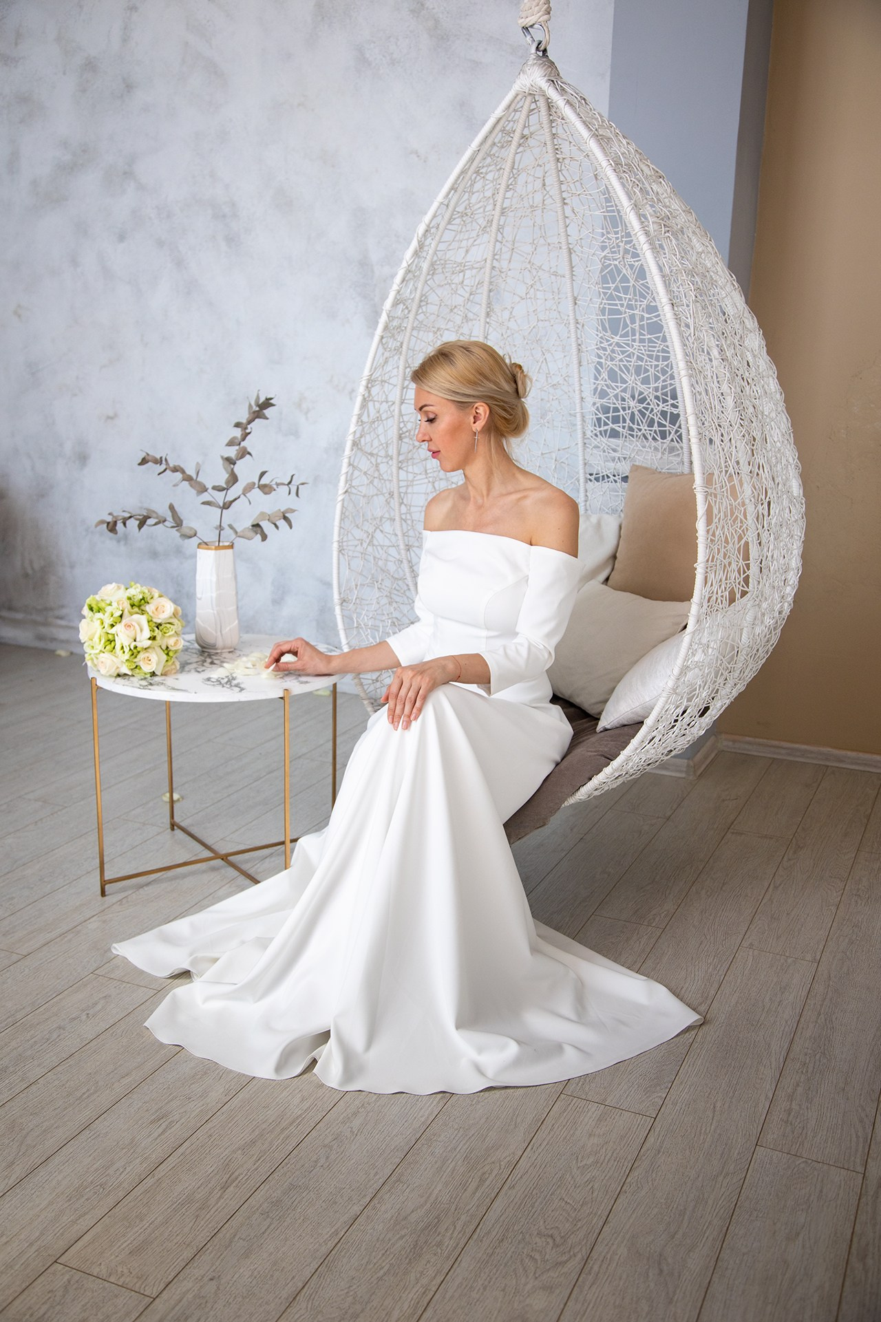 Студийная фотография невесты в белой качели коконе в красивом платье рядом со столом и букетом в Кемерово