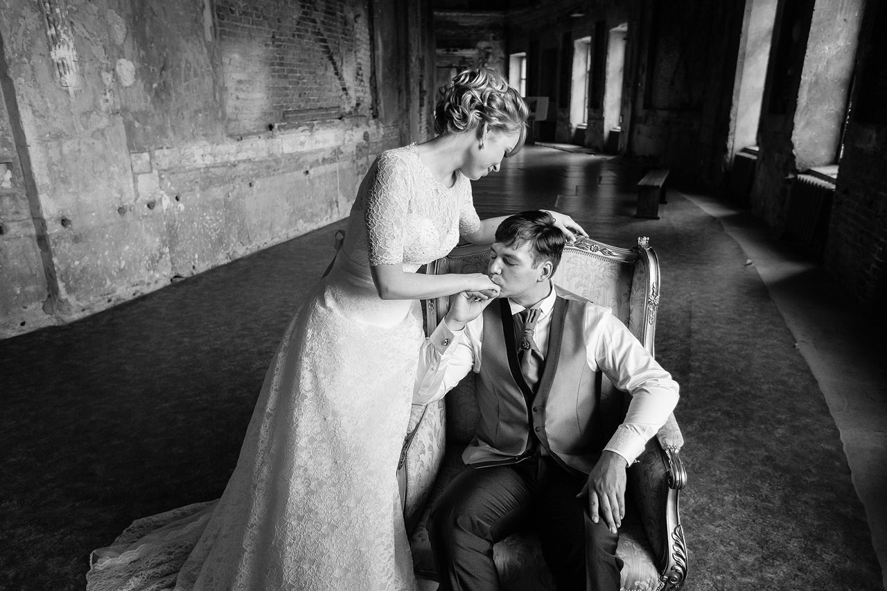 жених сидя в старинном кресле в зале гатчинского дворца целует руку невесты 