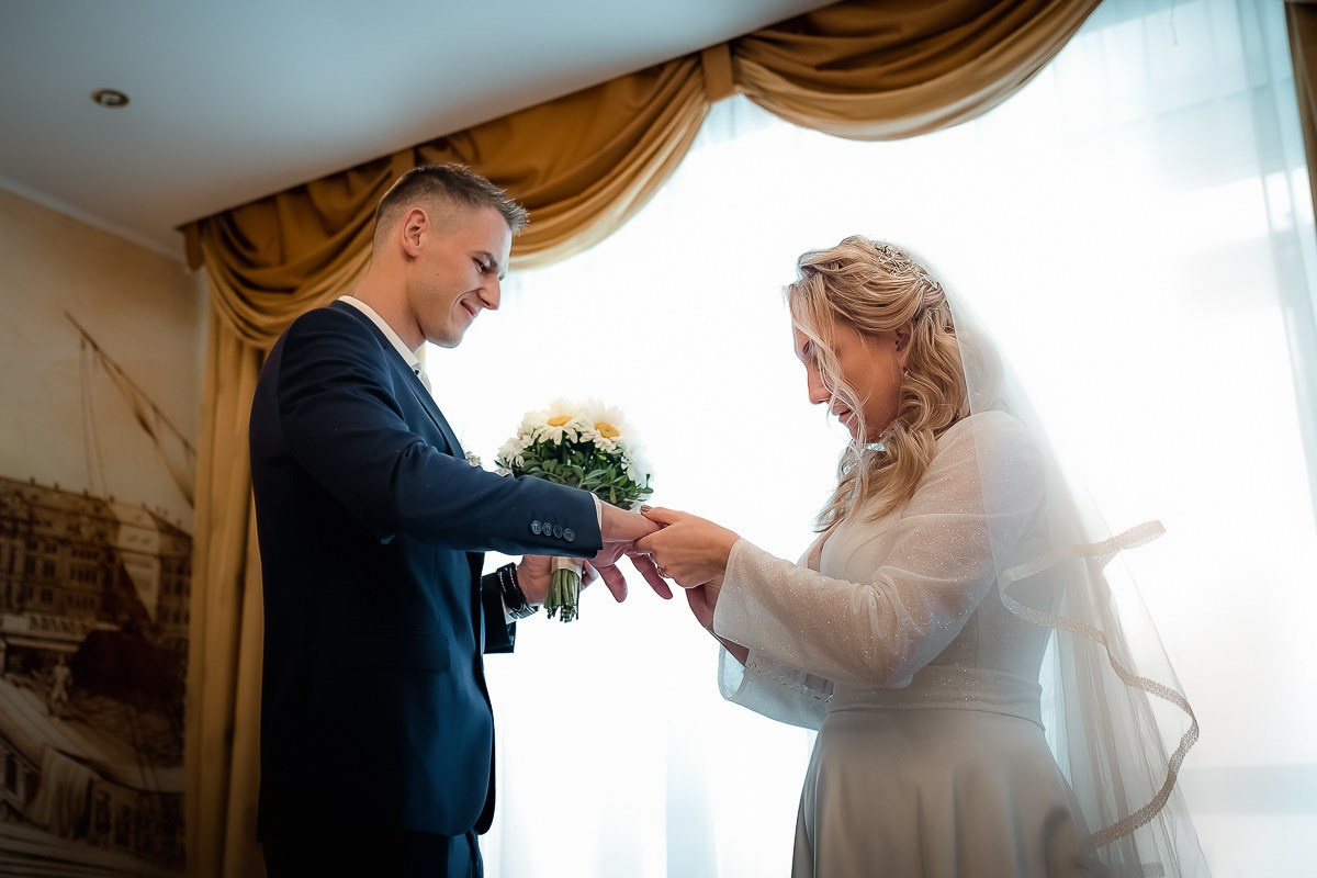 Невеста надевает жениху кольцо во время регистрации брака в ЗАГСе на Васильевском острове в Санкт-Петербурге.  Горизонтальный поясной кадр.