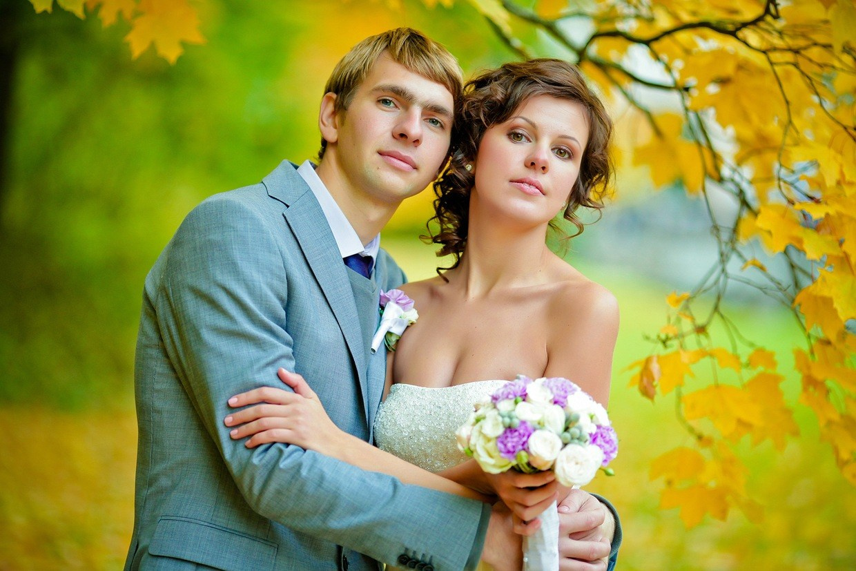 жених в сером костюме обнимает невесту с обнаженными плечами в осеннем парке