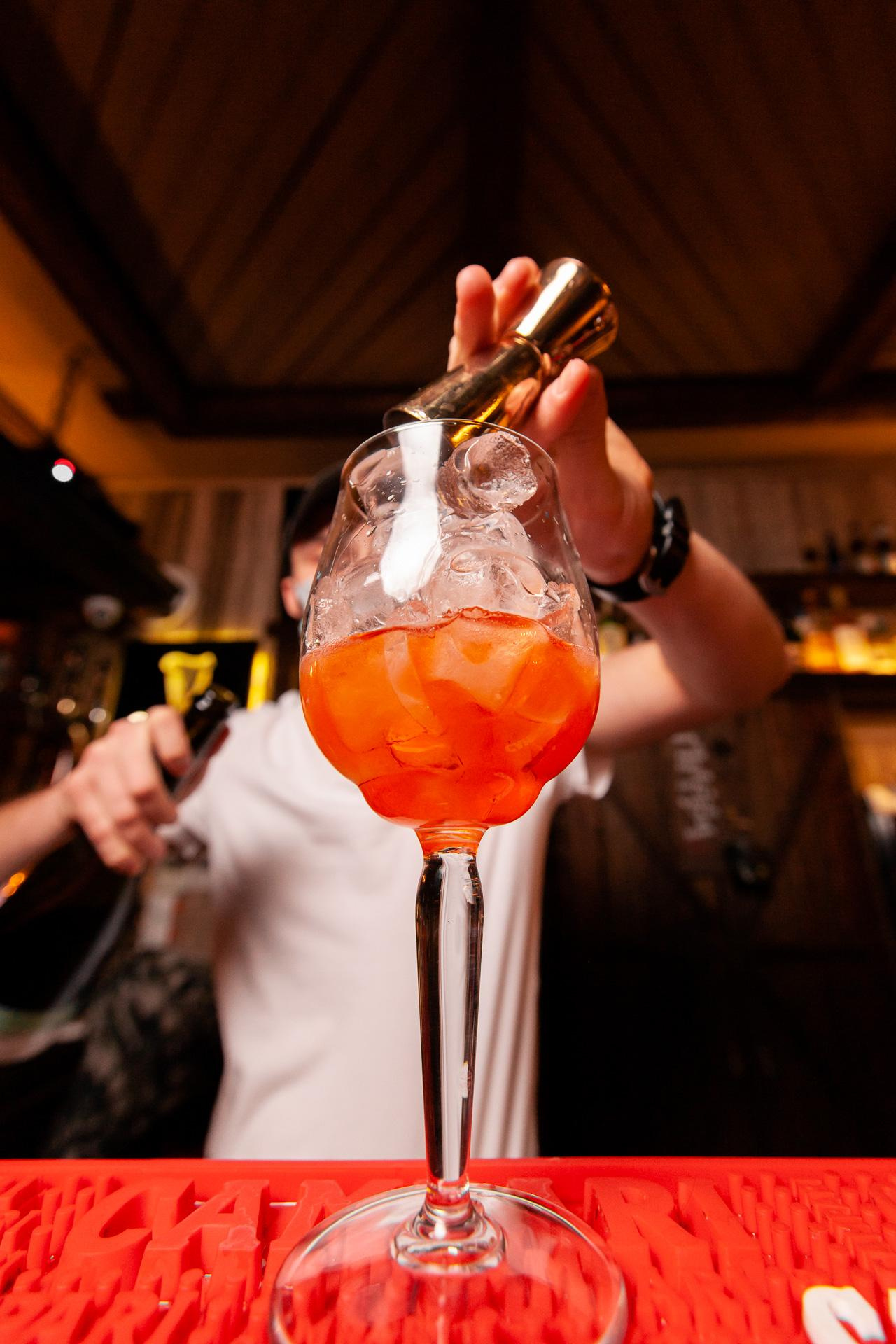 Бармен вливает Просекко в бокал с коктейлем Aperol Spritz