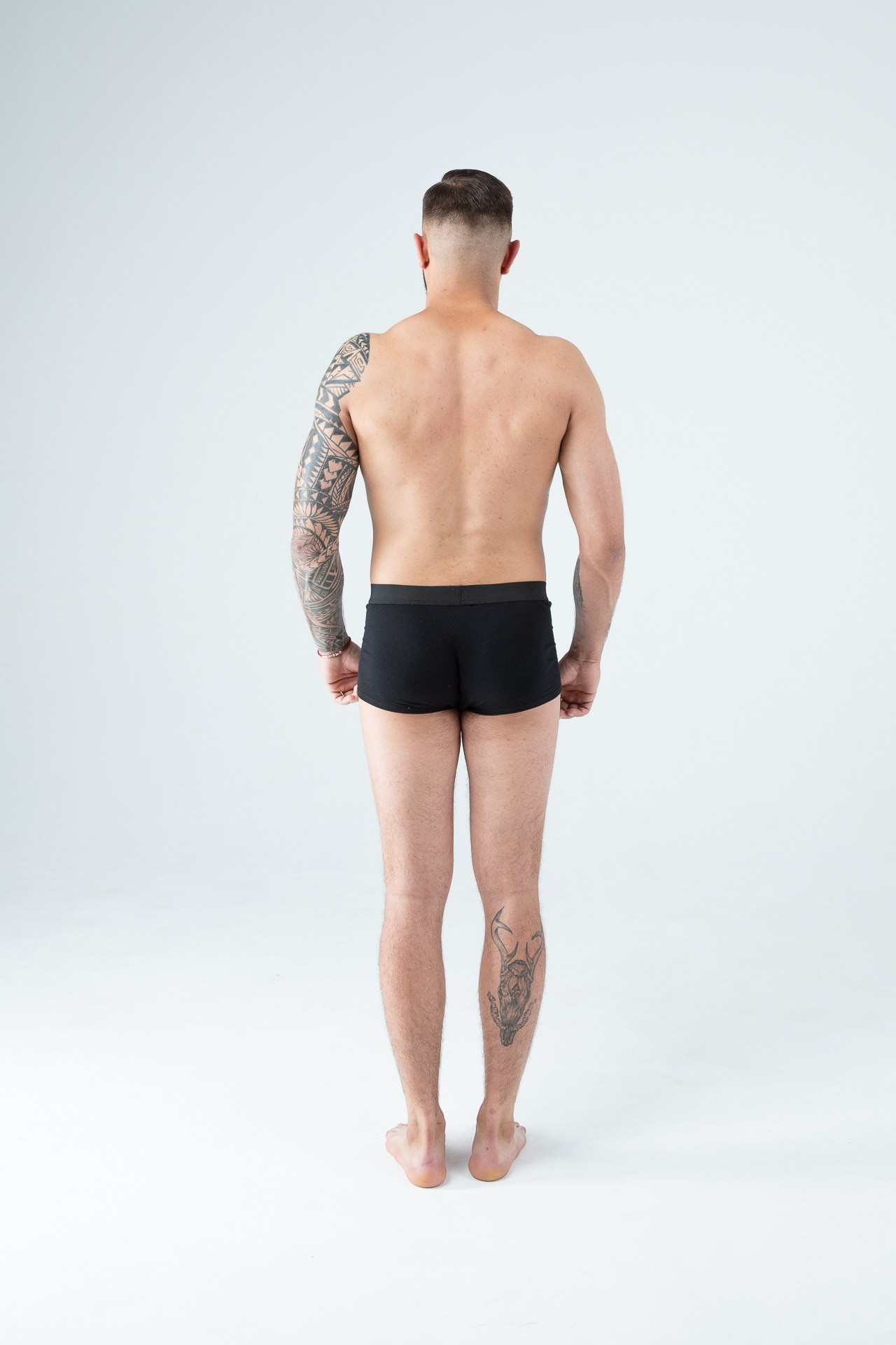 Мужчина модель с бородой с татуировками в черных трусах
