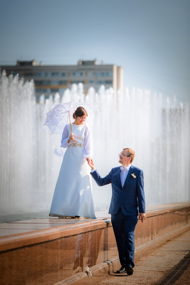 Жених и невеста идут вдоль фонтана у  ЗАГСа Красносельского района СПб