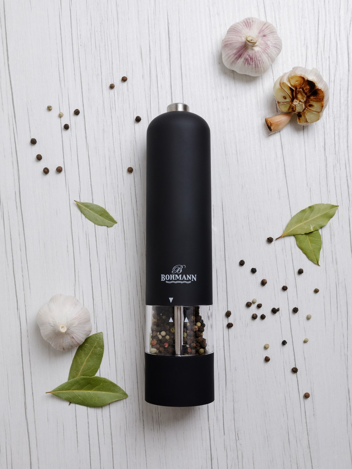 Автоматическая перечница лежит на белом столе в окружении специй