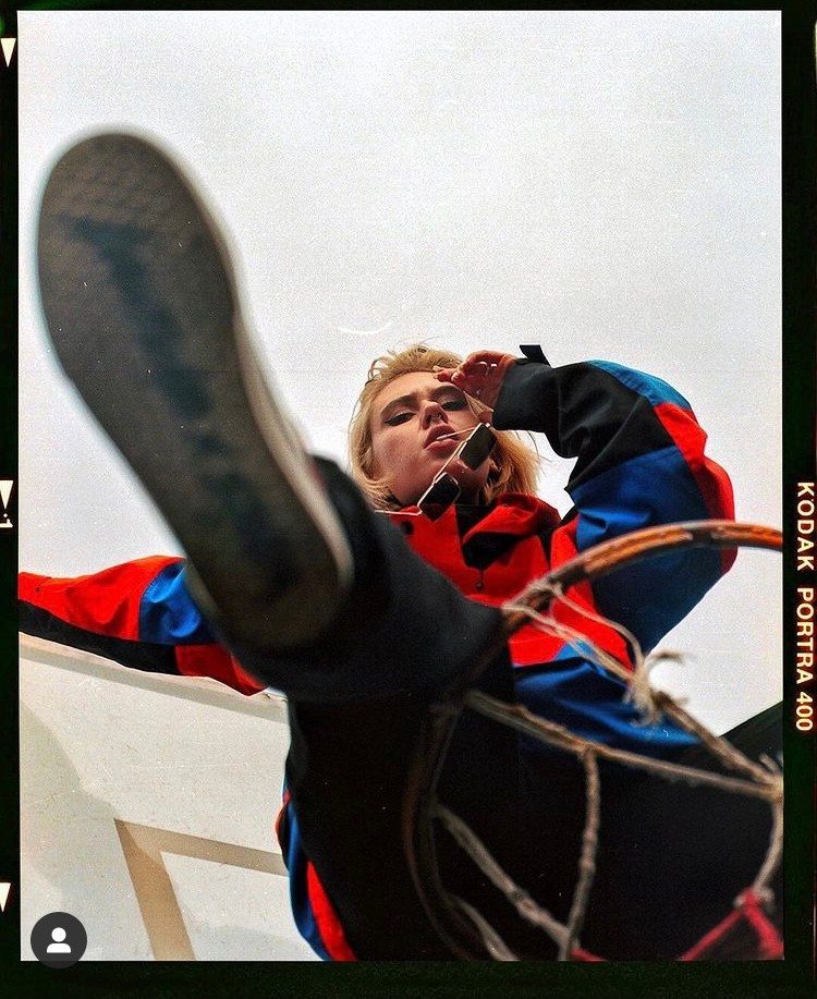 Танцовщица в красной куртке сидит на баскетбольном кольце