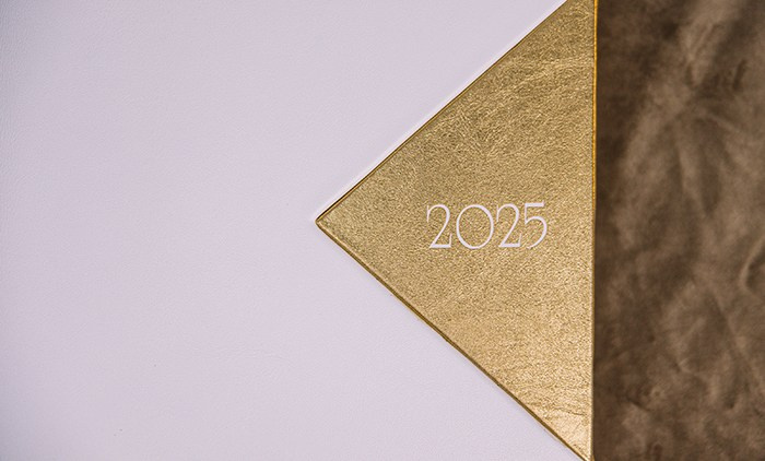 Макро-фото золотого тиснения цифр 2025 на фактурном золотом фоне. Угловой элемент белой фотокниги.