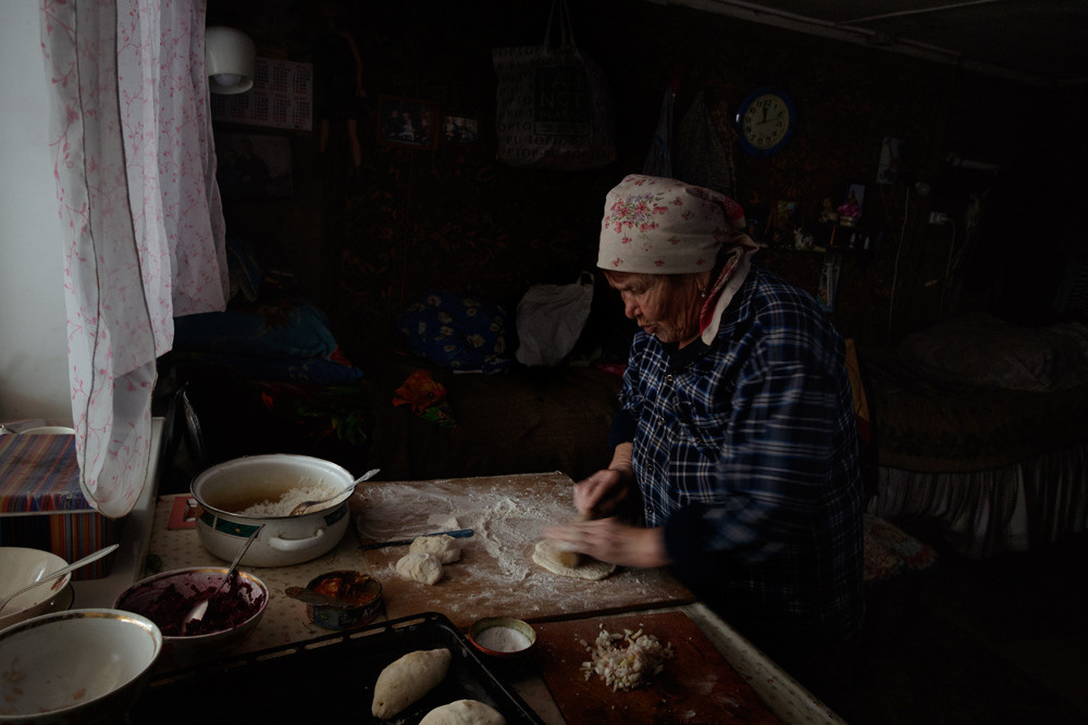 Бабушка делает пирожки у окна.