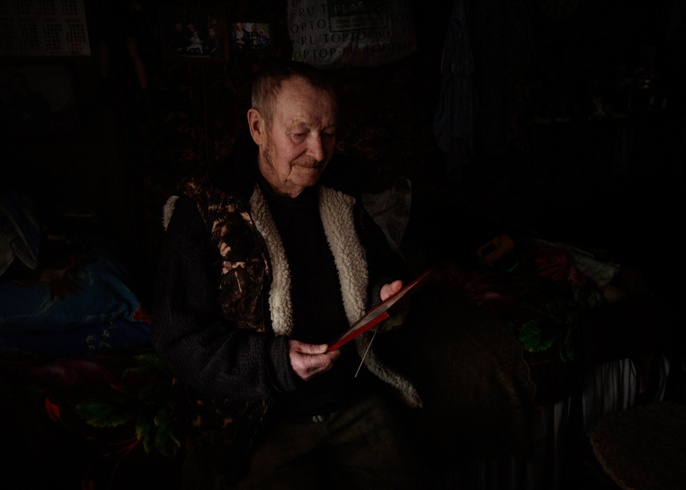 Дедушка смотрит фотографию в тёмной комнате.