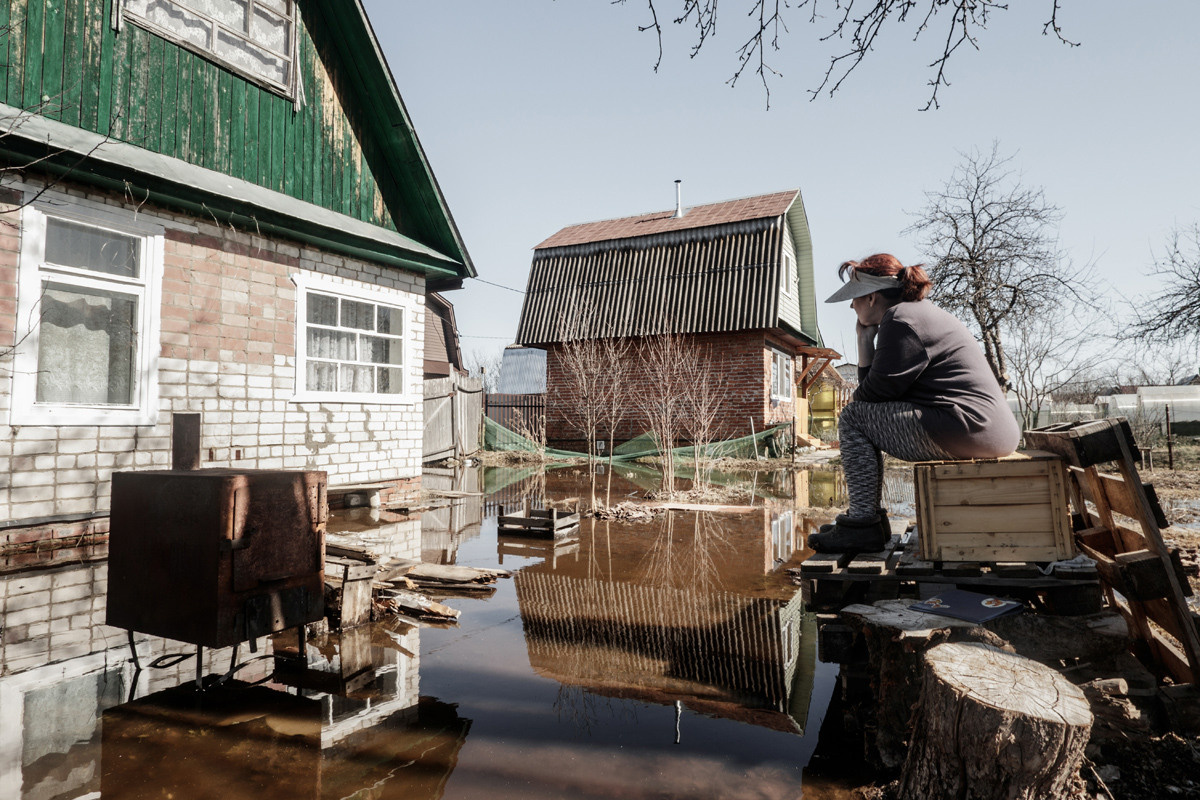 Женщина сидит на затопленном участке рядом с домом.