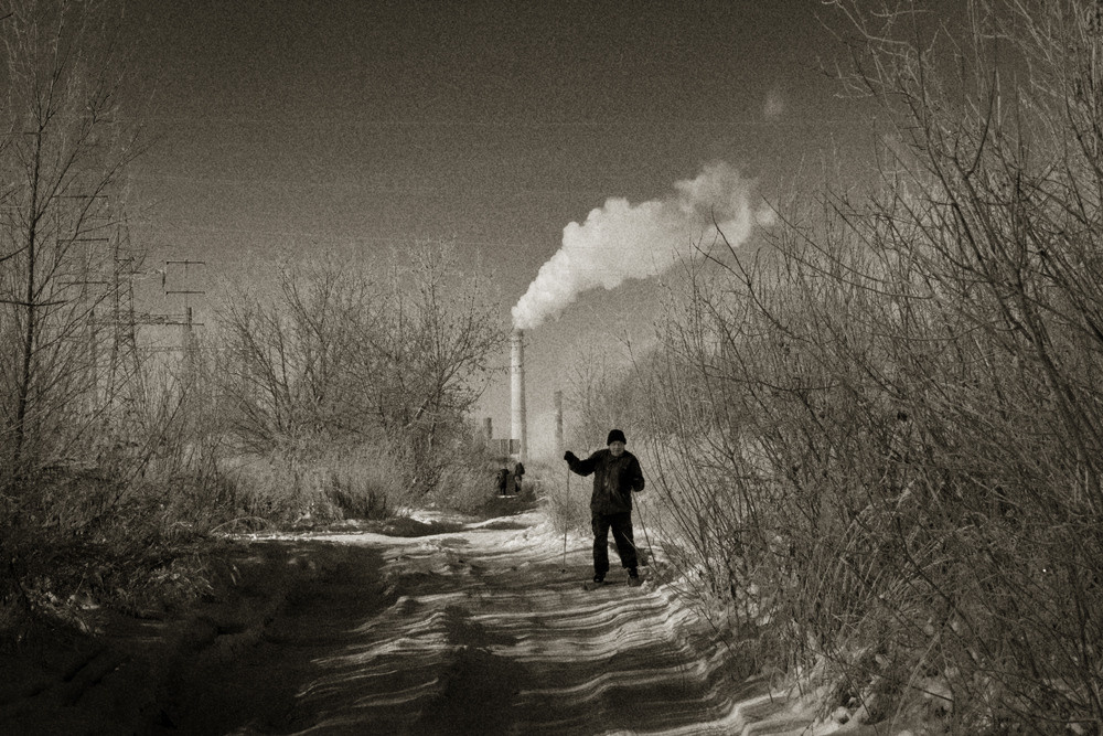 Мужчина на лыжах, на фоне трубы с дымом. Чёрно-белая фотография.