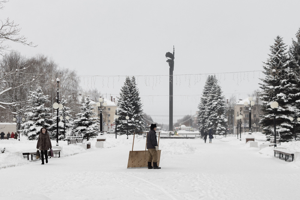 Убощик снега со скребком на фоне памятника военному с автоматом.