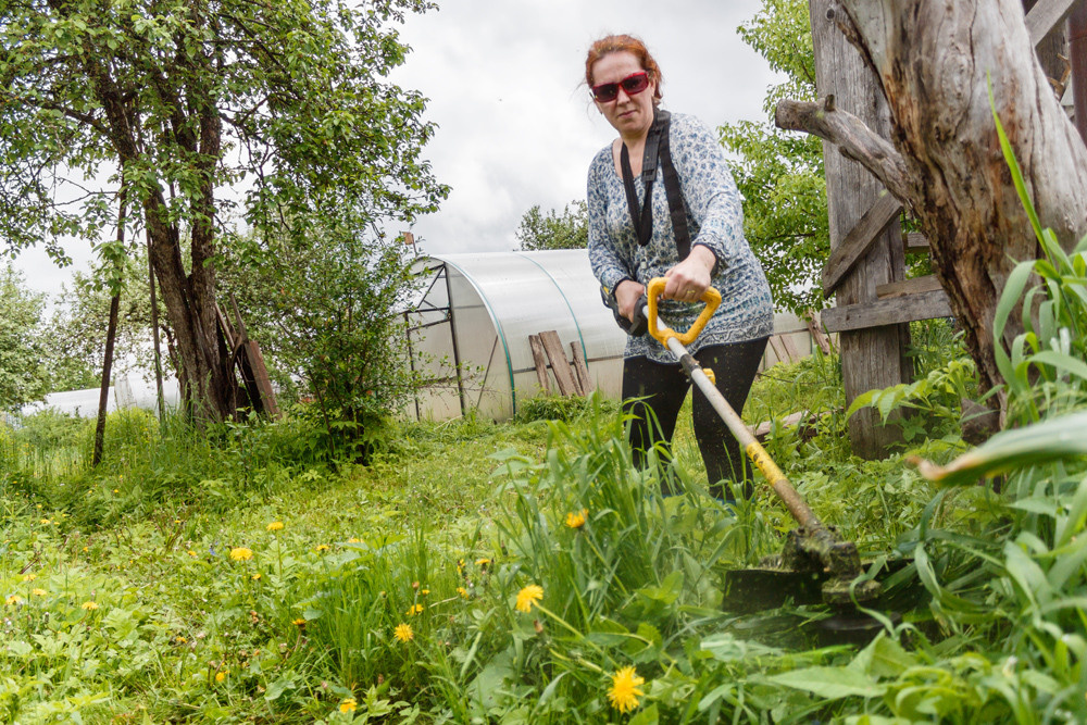 Женщина с газонокосилкой на садовом участке.