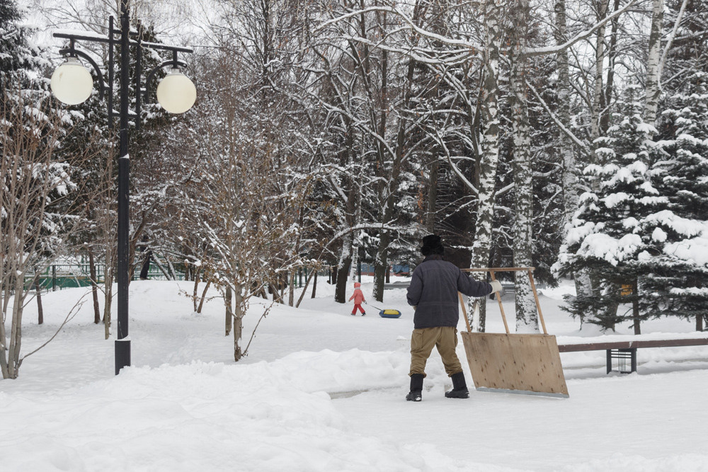 Мужчина убирает снег скребком в парке и смотрит на девочку с балоном.