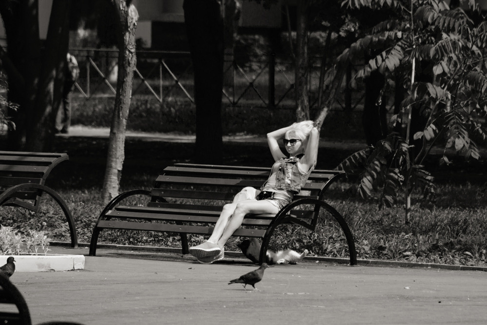 Девушка сидит на лавочке в парке и кошка играет под ней.