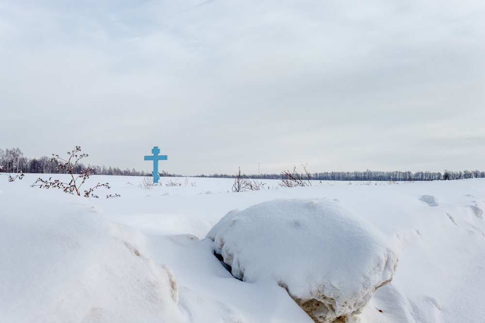 Голубой крест на обочине дороги, рядом снежный валун.