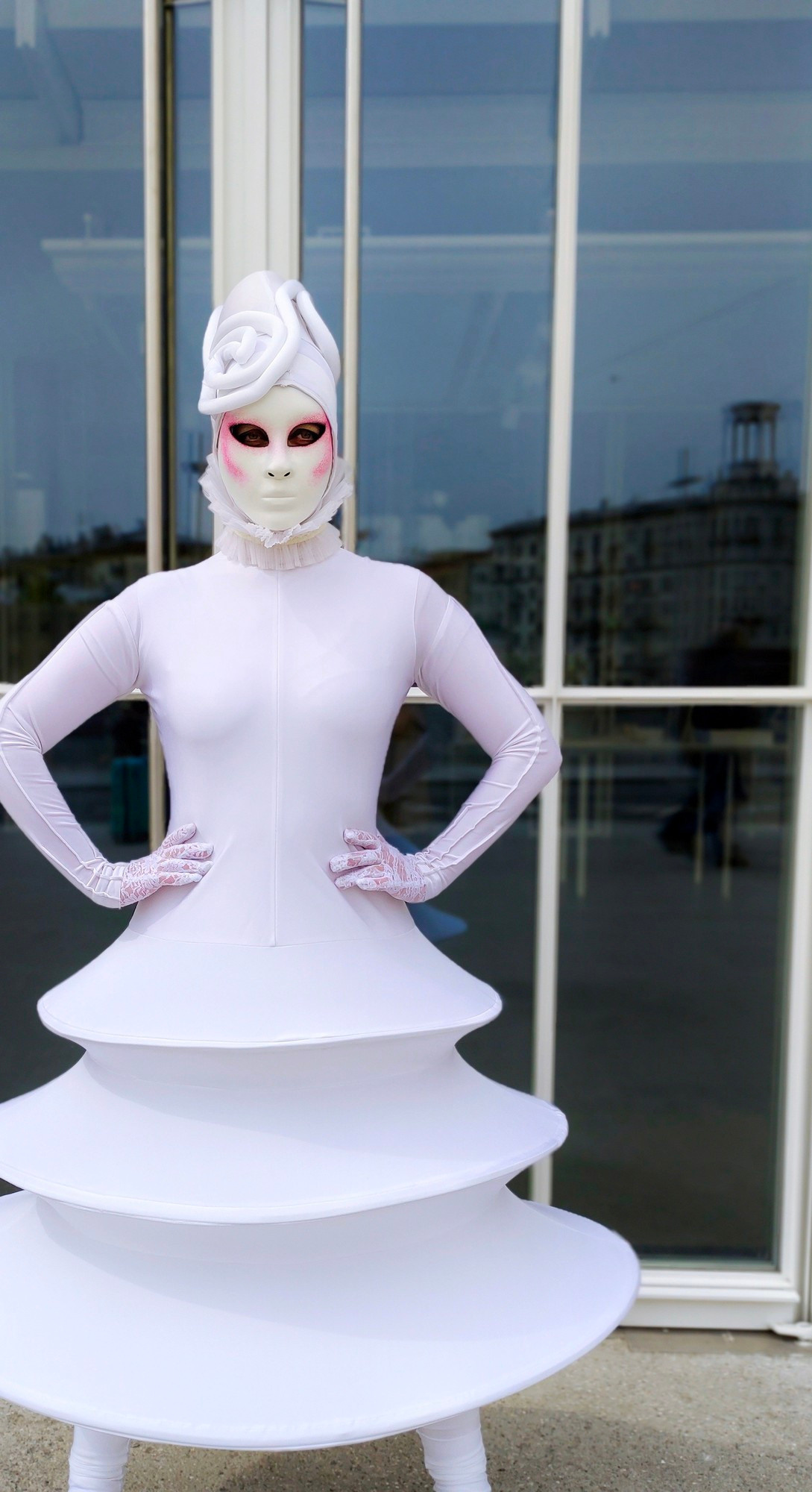 Персонаж мим в белом костюме позирует фотографу у белого здания.