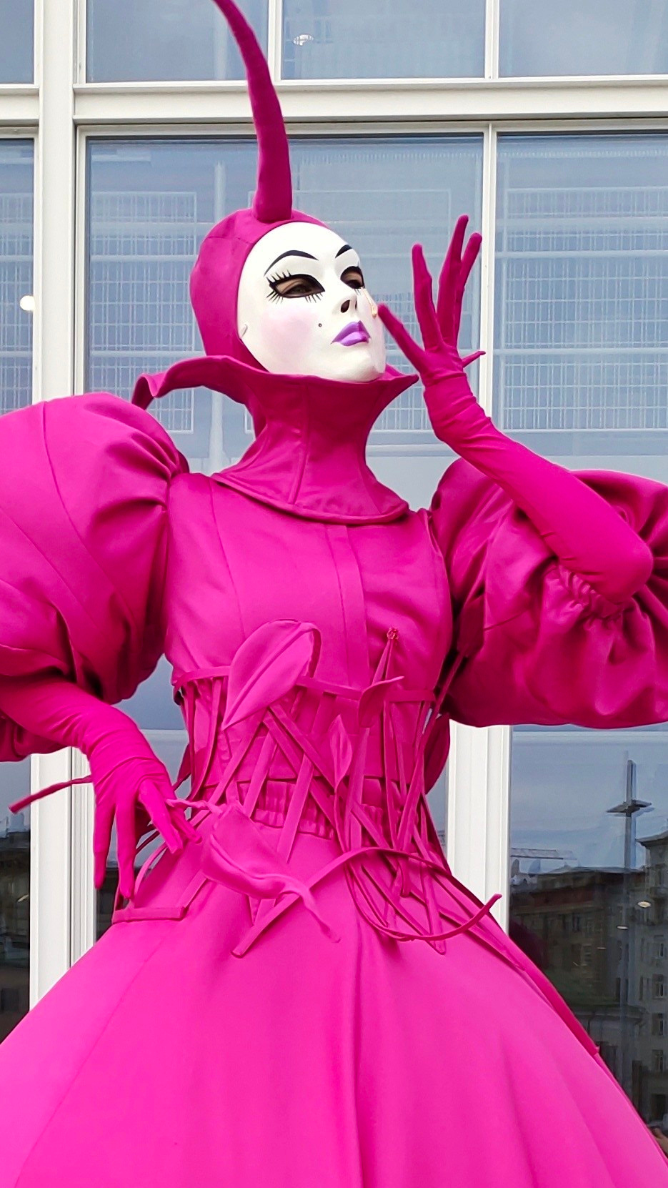 Мим поднёс руку к лицу и позирует фотографу на фоне окна.