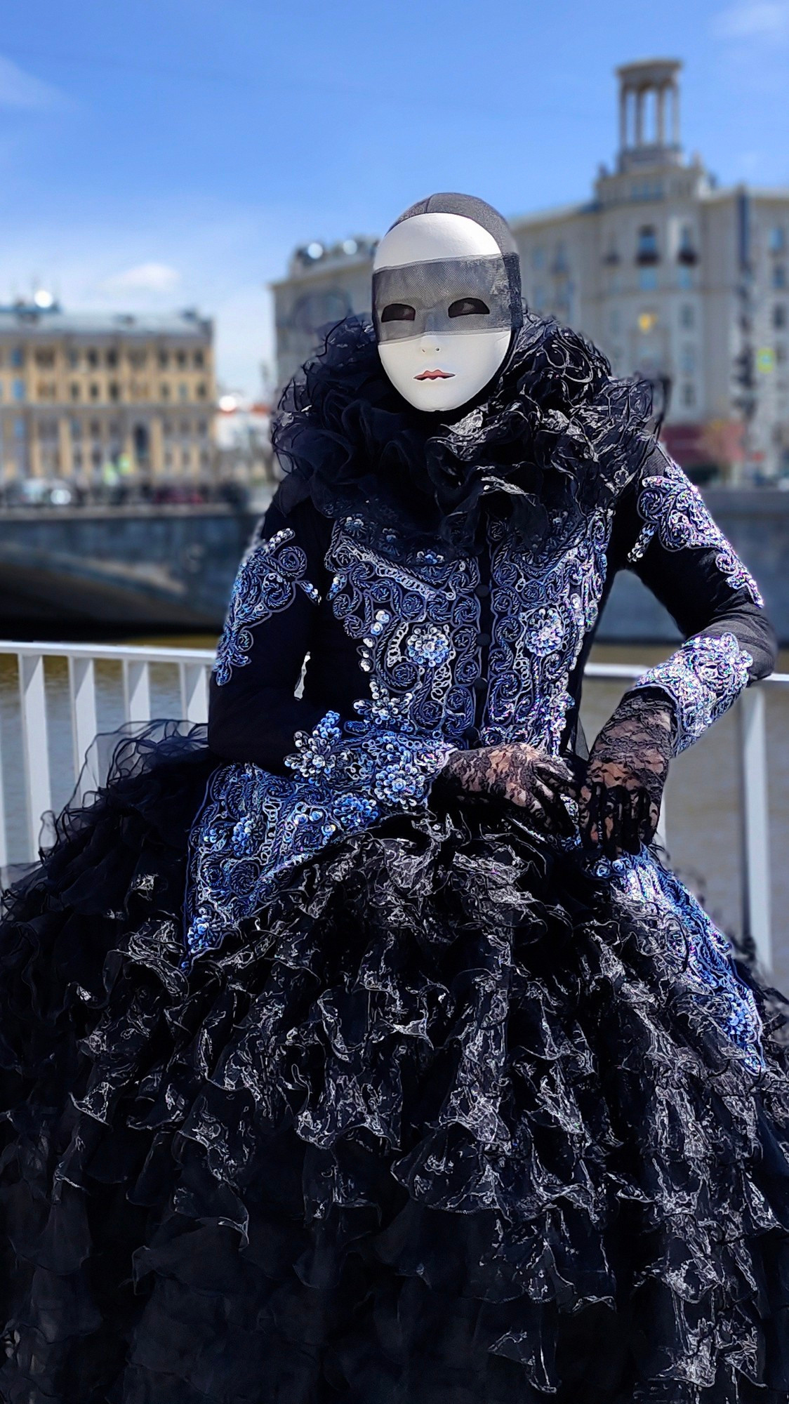 Мим чёрная Пешка в чёрном платье позирует фотографу на набережной реки Москва.