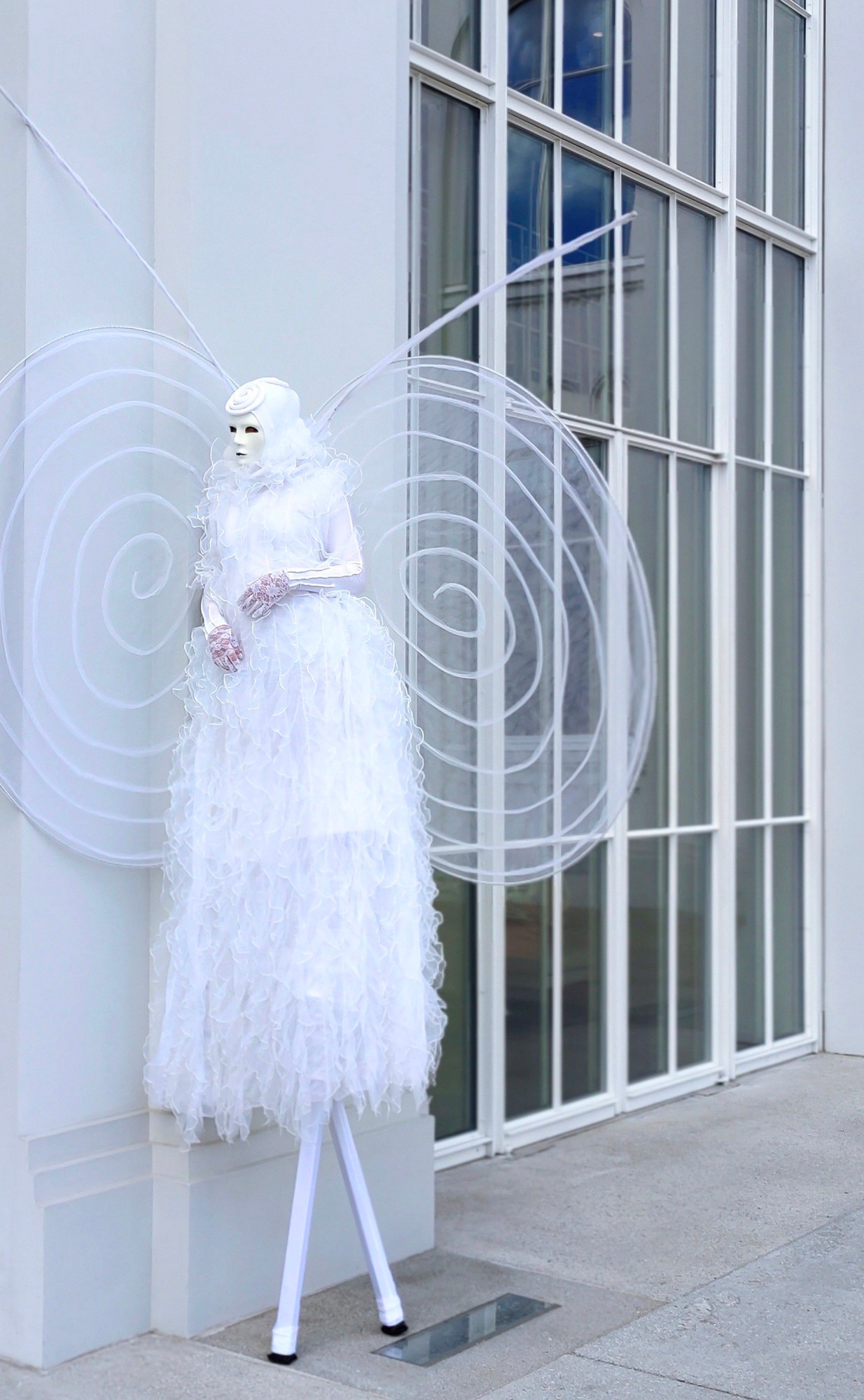 Ходулист в белом костюме облокачивается на стену ЗАГСа.