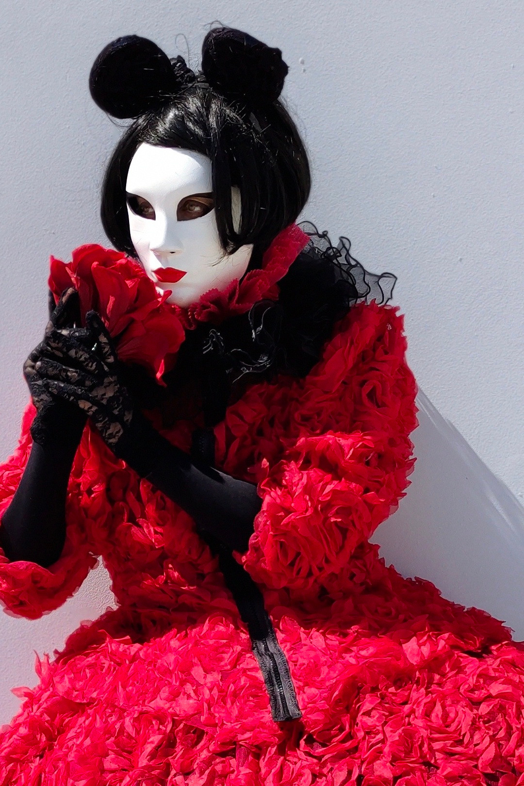 Мим с ушками как у Микки Мауса в красном платье стоит у белой стены на корпоративе.