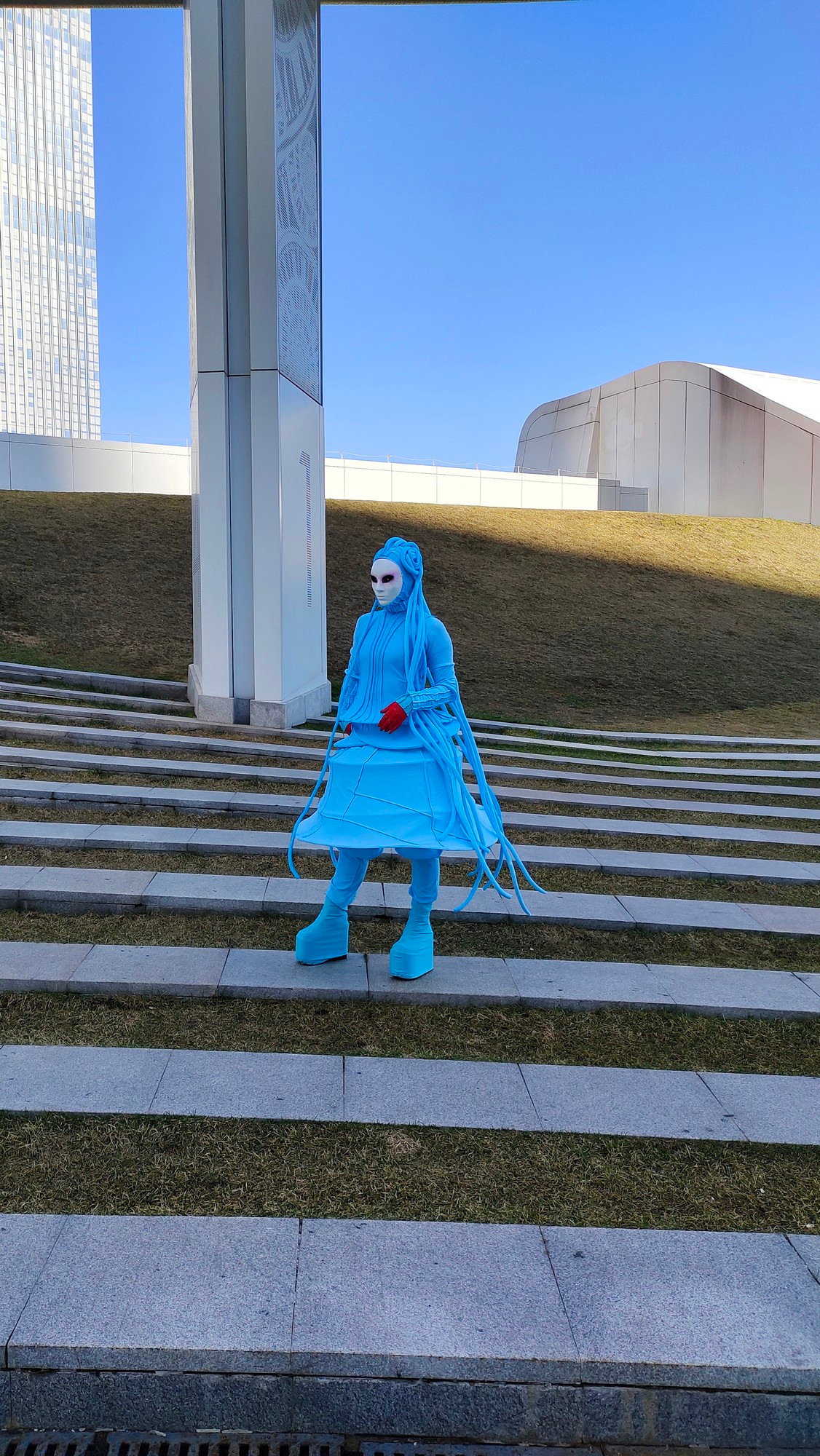 Мим в голубом костюме с дредами поднимается по огромной лестнице.