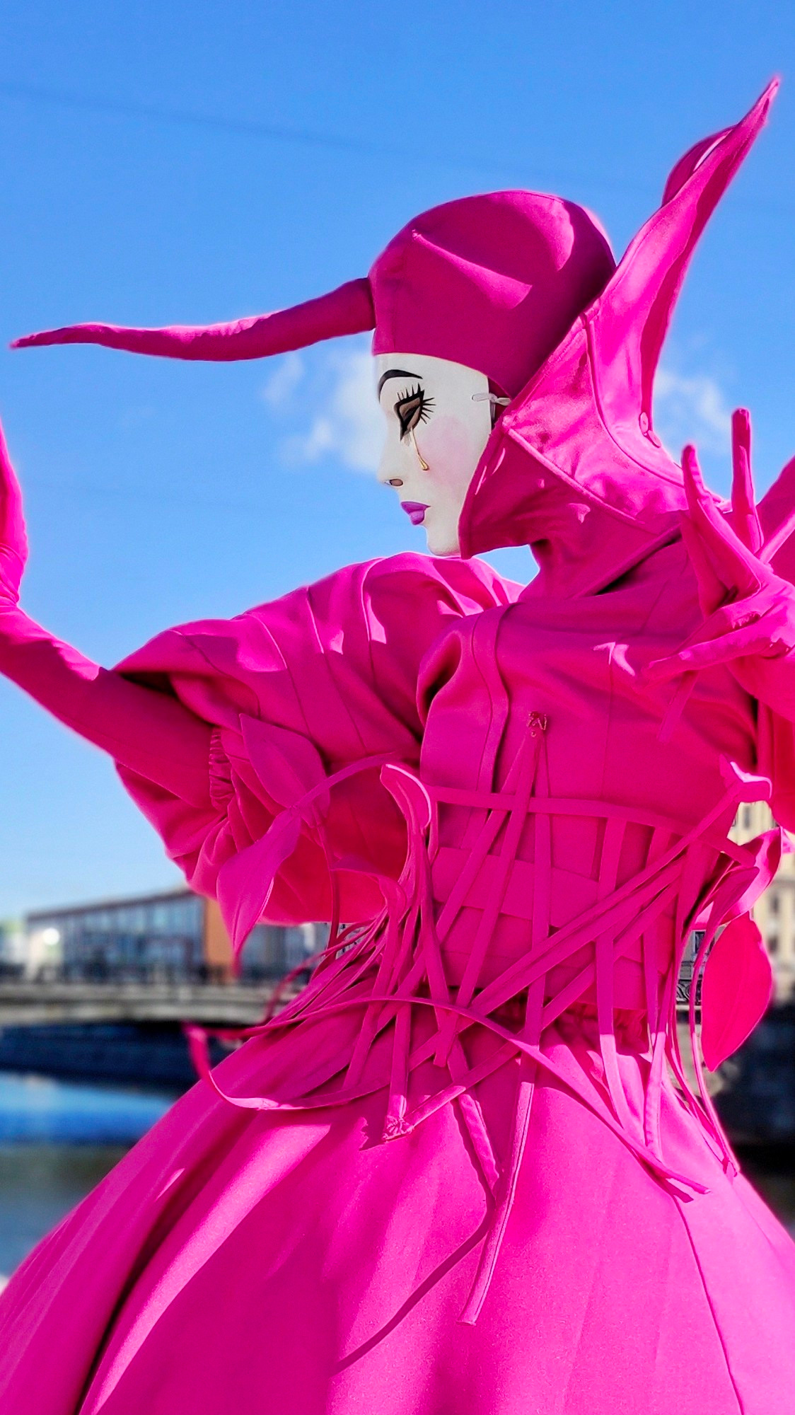 Мим в образе цветка в цвете фуксия на фоне голубого неба.