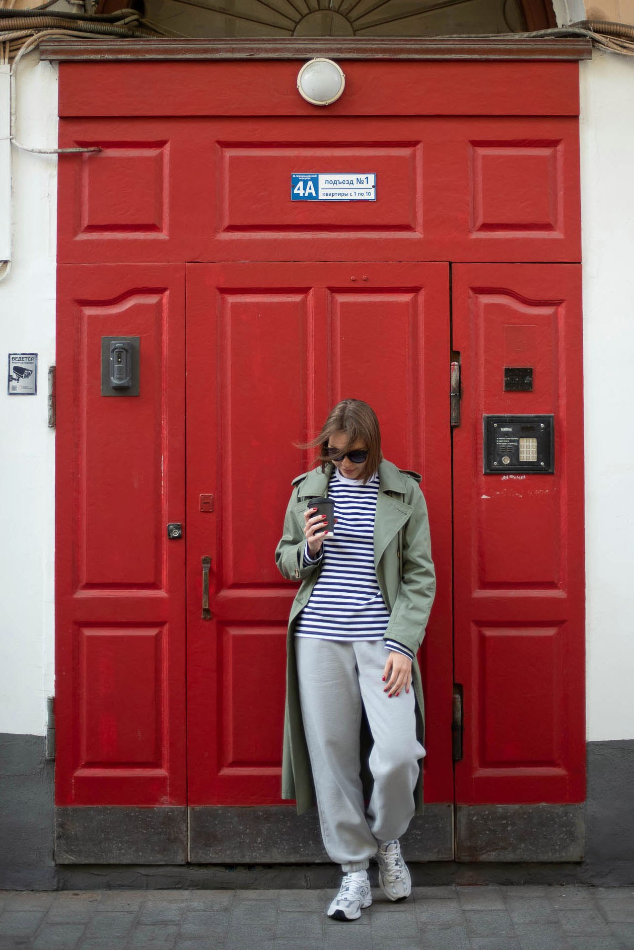 Молодая девушка в светлом костюме позирует на фоне ярко-красной двери — пример портретной и городской фотосъемки.