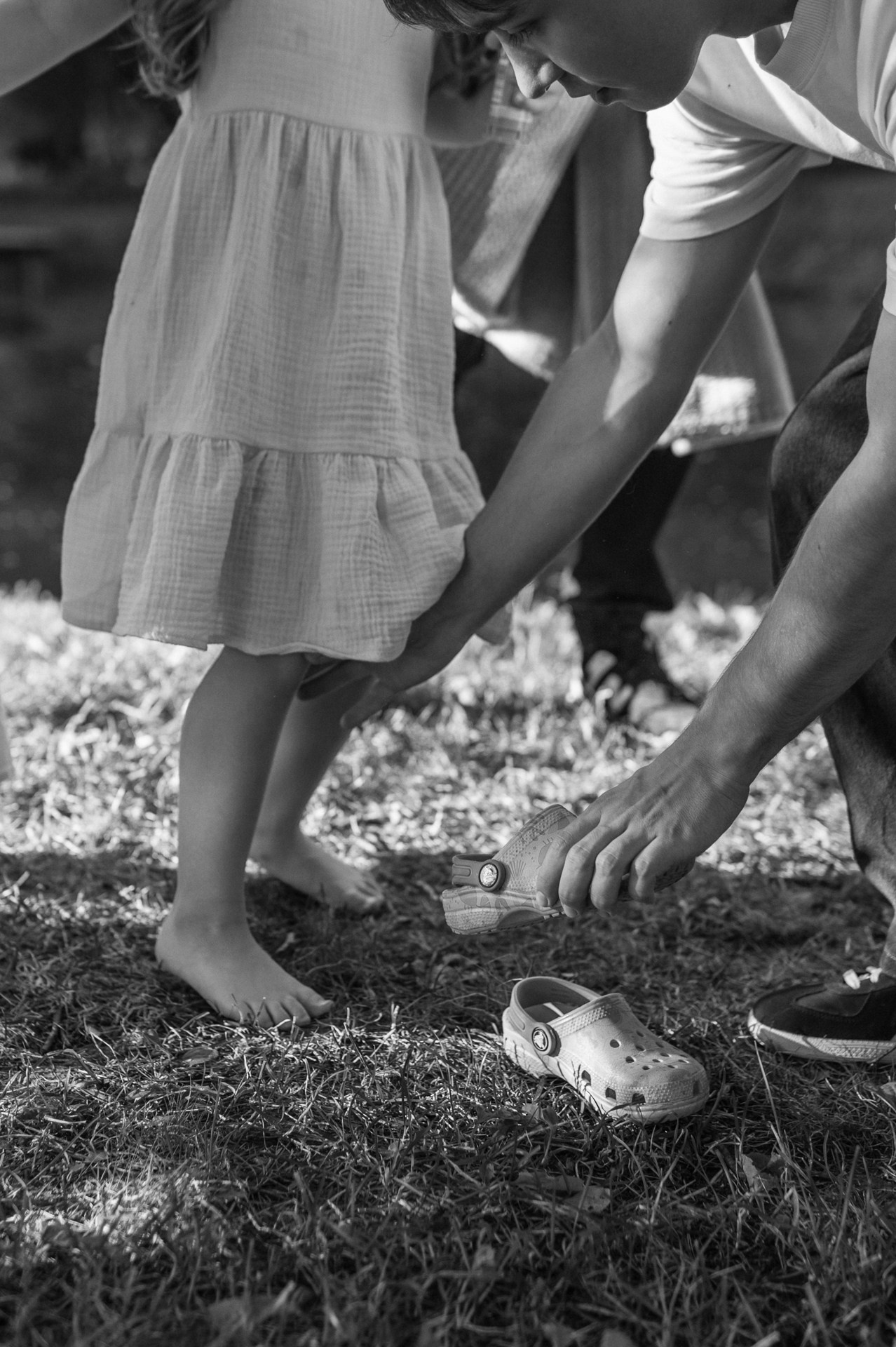 Черно-белое фото рук, которые надевают обувь. Мальчик обувает девочку в кроксы.