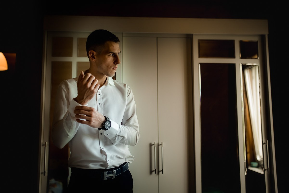 Жених застёгивает пуговицы рубашки и смотрит в окно в комнате в Санкт-Петербурге. Горизонтальный кадр