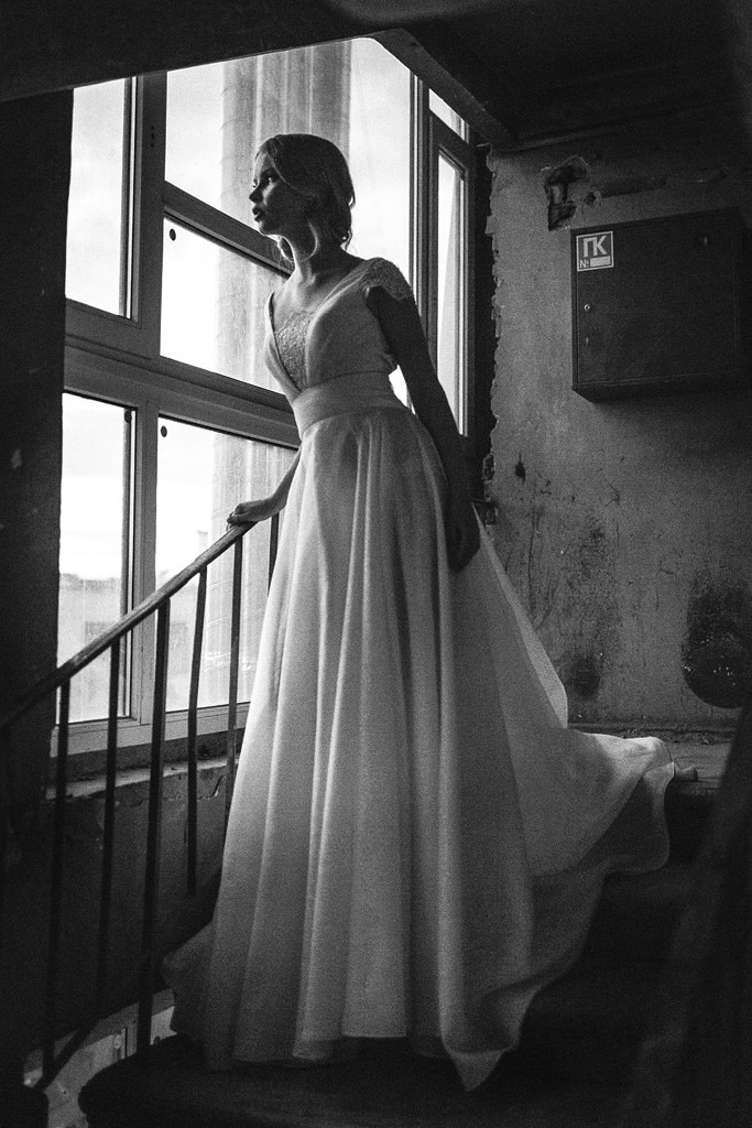 красивая блондинка в свадебном платье смотрит в окно в советском подьезде