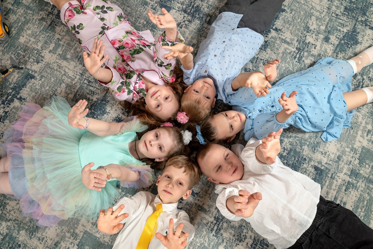 Детсадовцы лежат на ковре кружком и мило улыбаются фотографу.