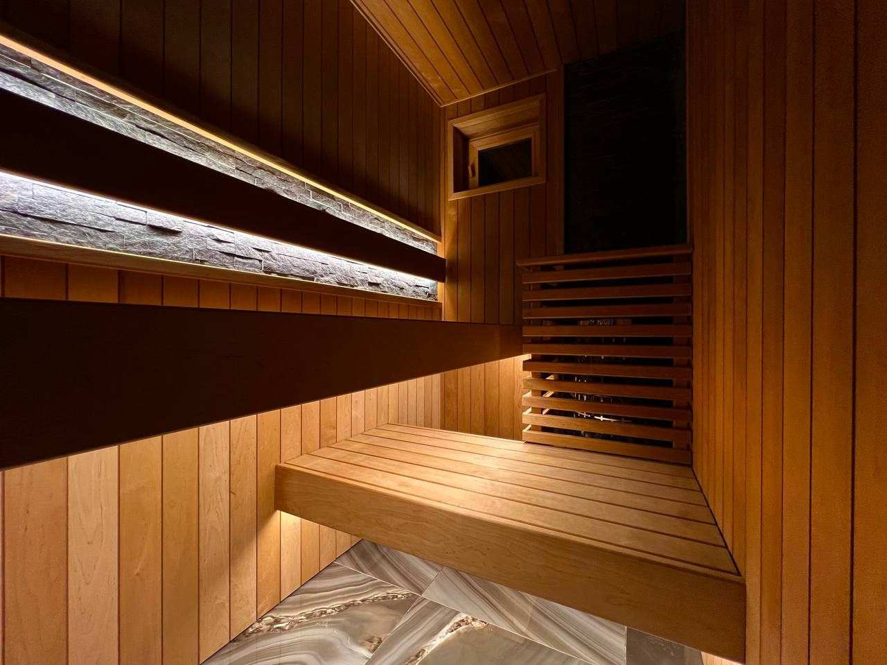 Семейная сауна в Охте: термоольха, природный камень и аккуратное реечное ограждение печи, защищающее любопытные детские ручки. SaunaTopMasters