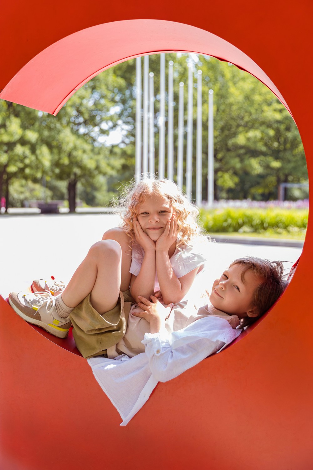 Девочка лежит в красной уличной инсталляции, сзади подружка- кудряшка.