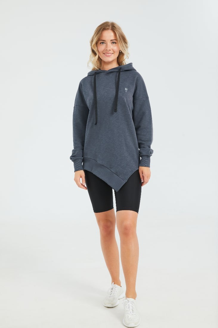 Девушка блондинка в сером худи и черных леггинсах стоит на сером фоне