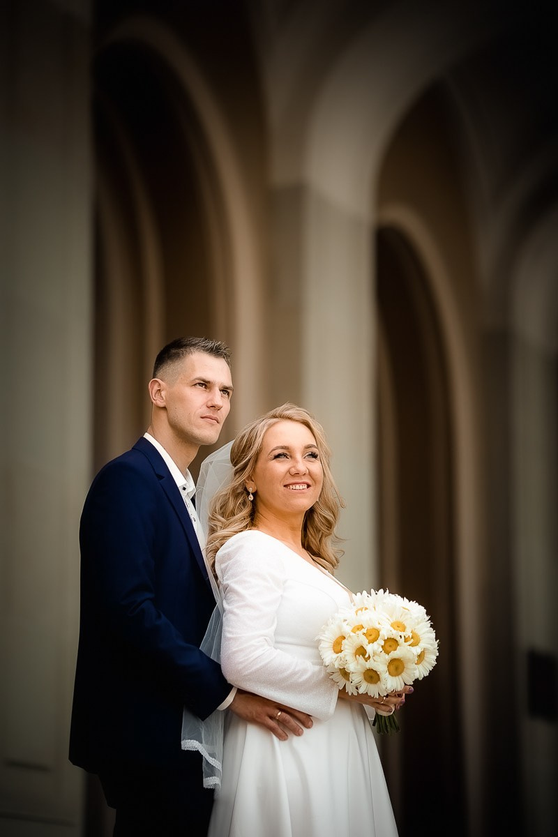 Жених и невеста смотрят в даль, стоя на крыльце заксобрания в Санкт-Петербурге. Вертикальный поясной кадр.