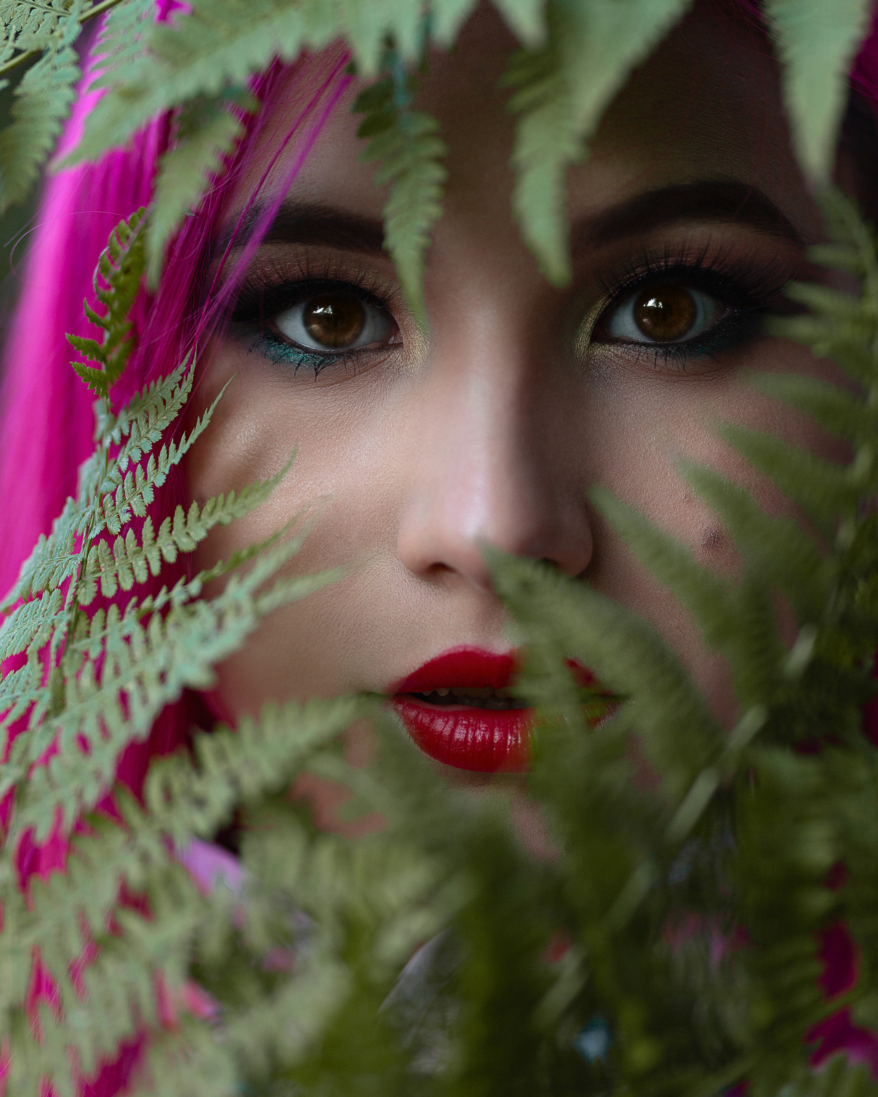 Портретный фотограф в Нижнем Новгороде. Необычные фотосессии в Нижнем Новгороде. Заказать фотосессию. Девушка азиатка с розовыми цветными волосами и красивыми глазами крупный портрет в листве.