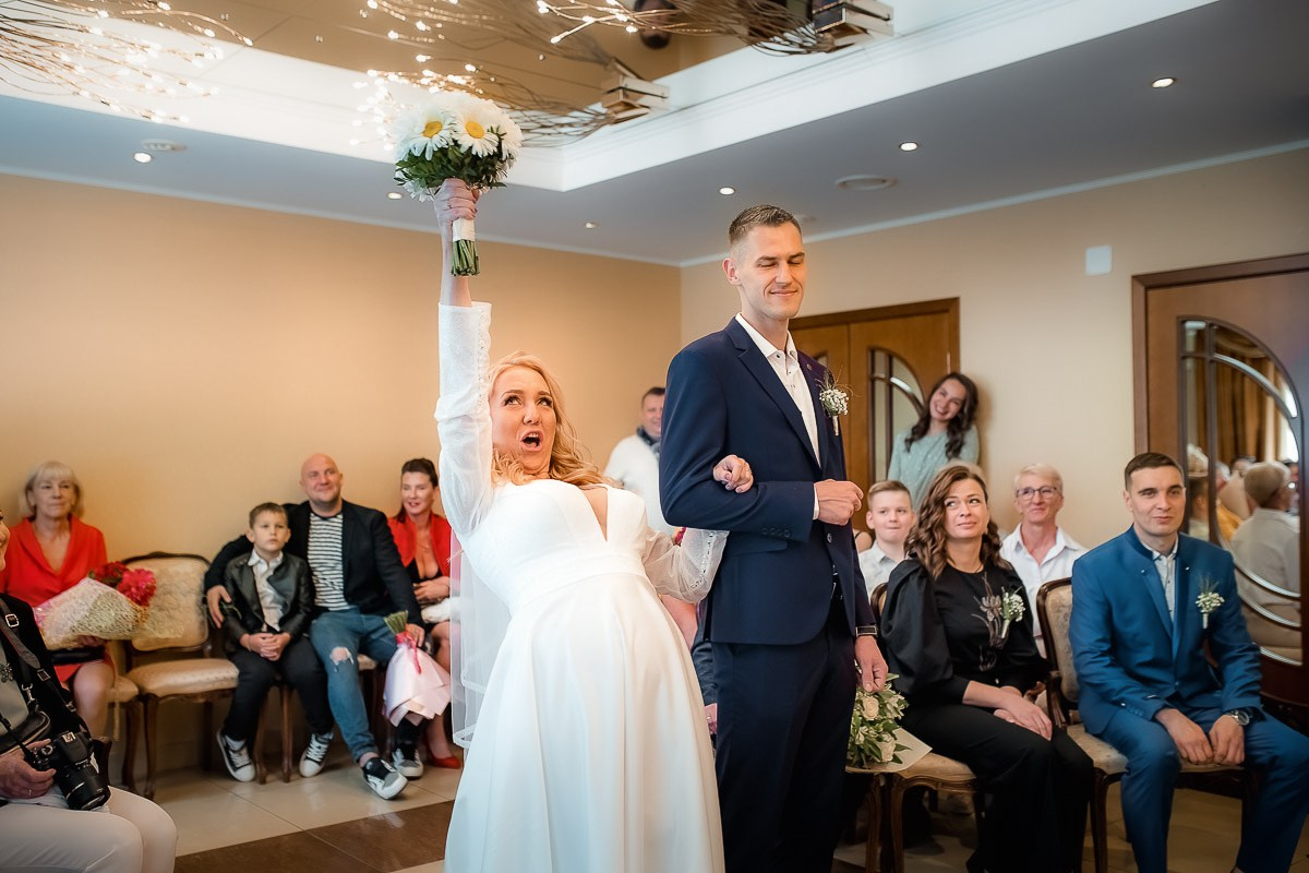 Жених и невеста стоят и смотрят на регистратора во время регистрации брака в ЗАГСе на Васильевском острове в Санкт-Петербурге. Невеста поднимает вверх свадебный букет. Горизонтальный поясной кадр.