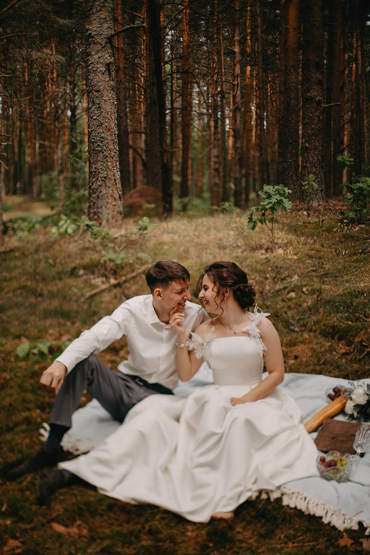 Пара сидит рядом на пляже, нежно обнявшись, словно время остановилось на этой идиллической свадебной фотографии